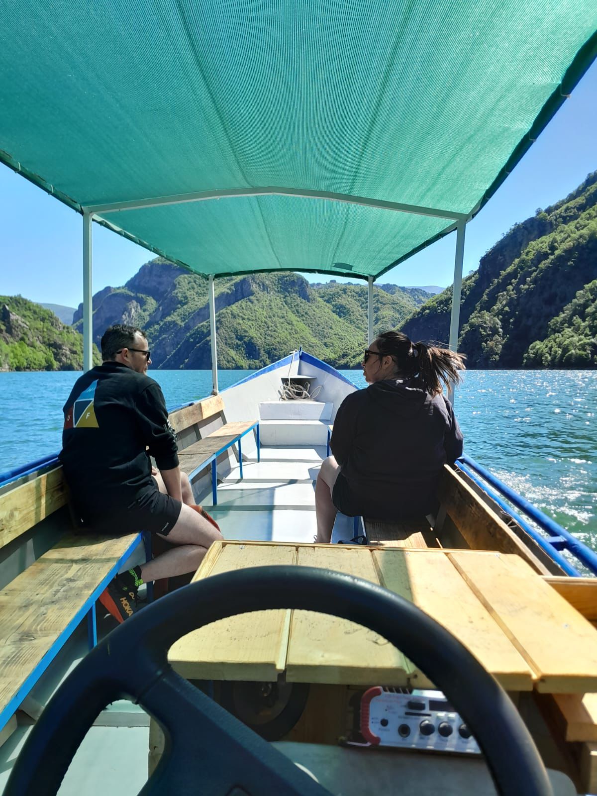 Boat cruising through the emerald waters of Lake Koman surrounded by steep mountain cliffs